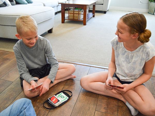 Kids sitting on the ground using The Card Buddy to play a card game- Uno