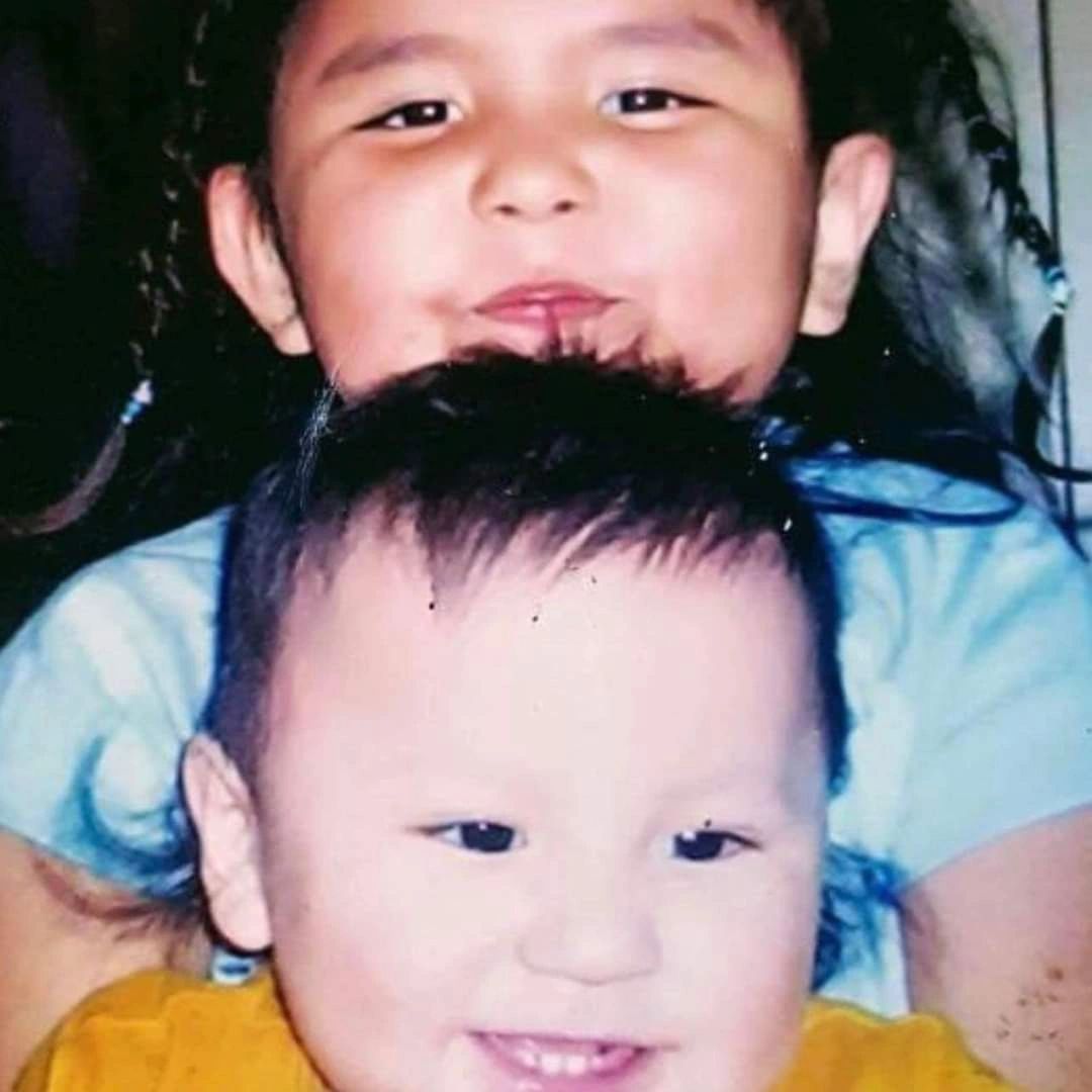 Two smiling children close together, one behind the other.