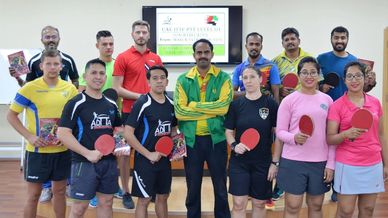 Group of table tennis players posing with paddles indoors.