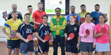 Group of table tennis players posing with paddles indoors.