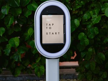 A photo booth screen with 'TAP TO START' displayed, surrounded by a ring light.
