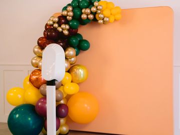 Colorful balloon arch decoration beside a peach backdrop and white stand.