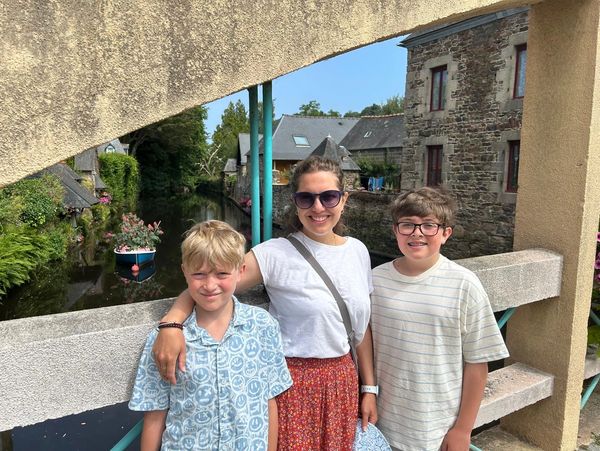 A woman and two boys smiling on a scenic bridge over a canal with stone houses.