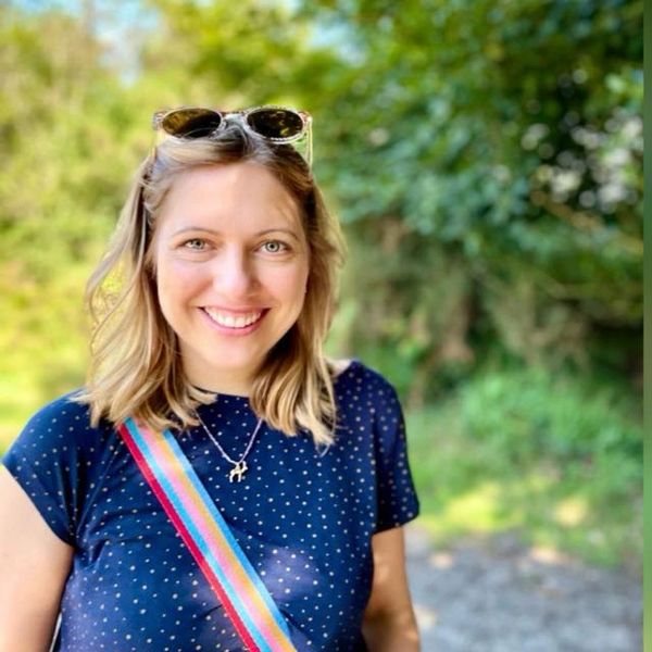 Smiling woman outdoors with sunglasses on her head and a colorful strap across her shoulder.