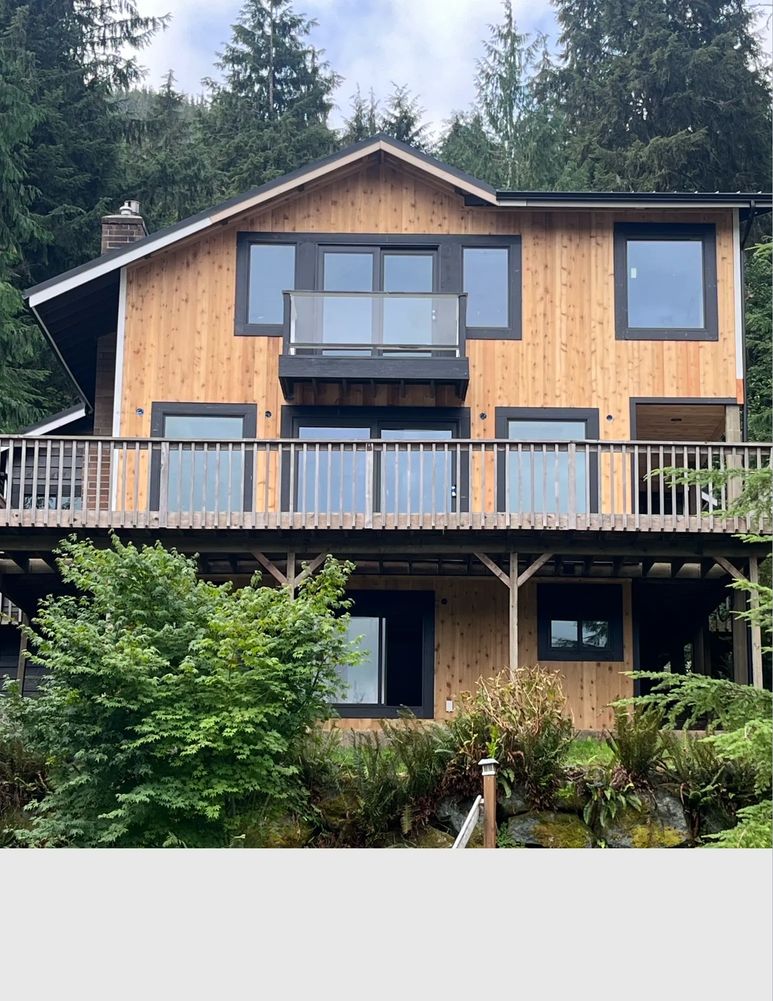 Modern wooden house with large windows and a balcony in a forested area.