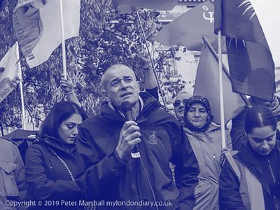 A man speaks into a microphone at a protest rally with supporters holding flags.