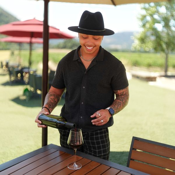 Man in black hat pouring wine outdoors.