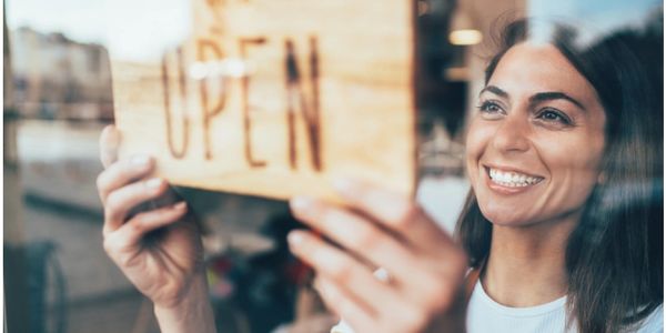 A woman placing an open sign in the front door of a small business. 