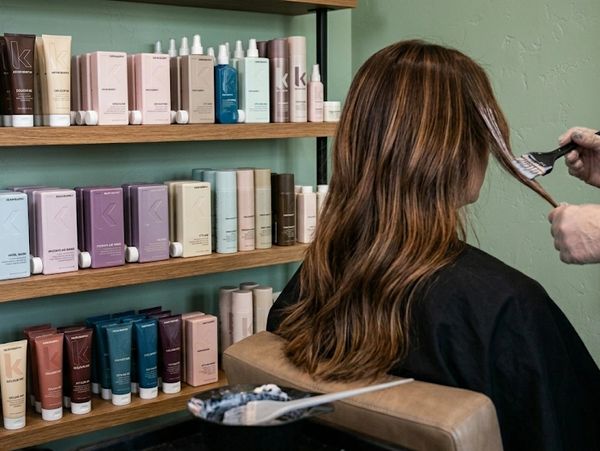 A woman getting her hair colored in a salon with hair products displayed on shelves.