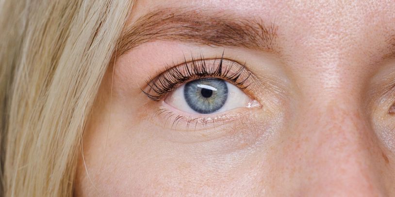 Close-up of a blue eye with long eyelashes and blonde hair.