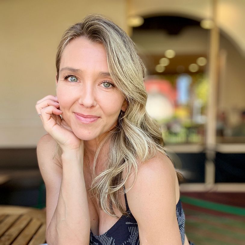 Woman with blonde hair smiling gently, resting her face on her hand.