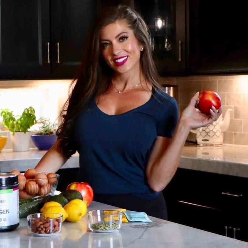Woman in kitchen holding an apple, surrounded by healthy foods.