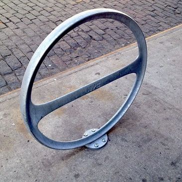 Metal circular bike rack on a city sidewalk with cobblestone street.