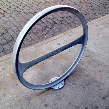 Metal circular bike rack on a city sidewalk with cobblestone street.