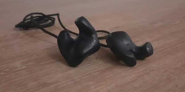 Black custom-molded earplugs on a wooden surface.