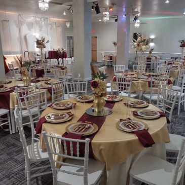 Beautiful gold and burgundy chargers, silverware, and napkins with chairs at a wedding reception.