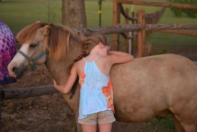 A girl hugs a brown pony outdoors.