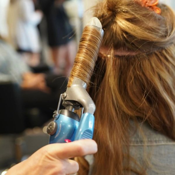 A person curling long hair with a blue curling iron.