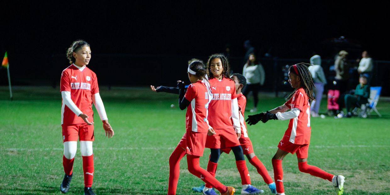 Young soccer players in red uniforms celebrating on the field at night.