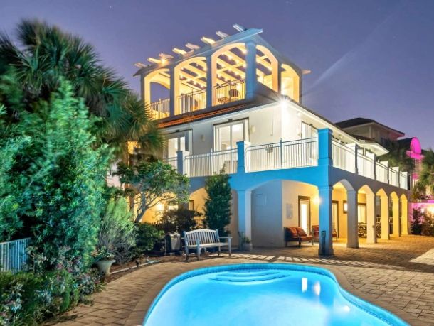 A well-lit modern house with a swimming pool at night.