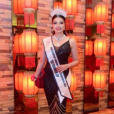 Beauty queen in a black gown with a crown and sash.