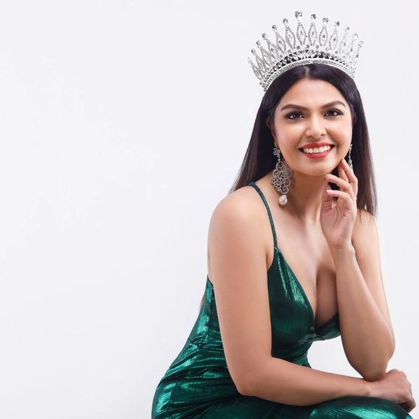 A smiling woman in a green dress wearing a sparkling crown and earrings.
