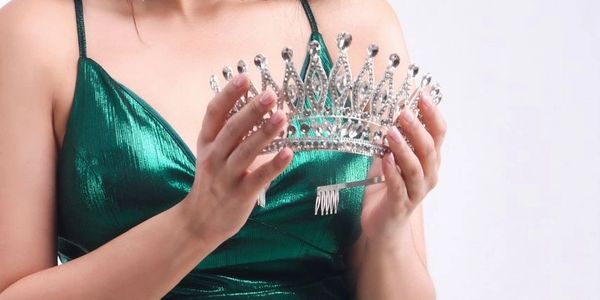 Woman in green dress holding a silver crown.