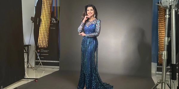 Woman in a sparkling blue gown posing in a professional photo studio setup.