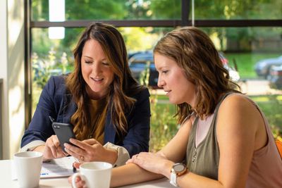 Two women discussing something on a smartphone in a cozy cafe.
