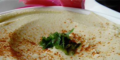 Close-up of hummus topped with paprika and parsley, with pickled vegetables.