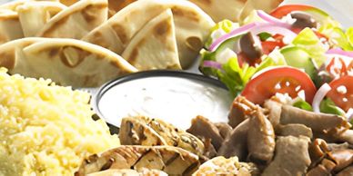 A platter with rice, pita bread, salad, grilled meat, and a dipping sauce.