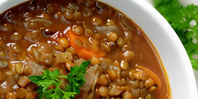 Close-up of a bowl of hearty lentil soup with carrots and herbs.

