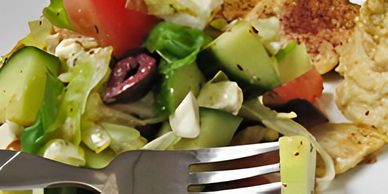 Fresh garden salad with cucumber, tomato, olives, and feta, next to pita bread.