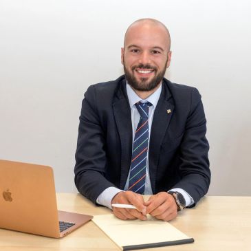 Uomo sorridente in giacca e cravatta alla scrivania con laptop.