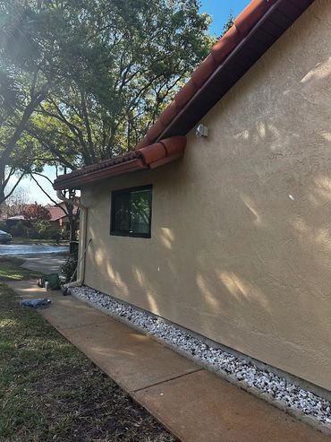 Side view of a beige house with a red-tiled roof and white decorative stones.