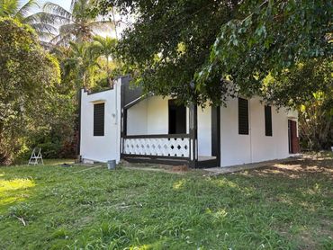 Small white house surrounded by greenery and trees.