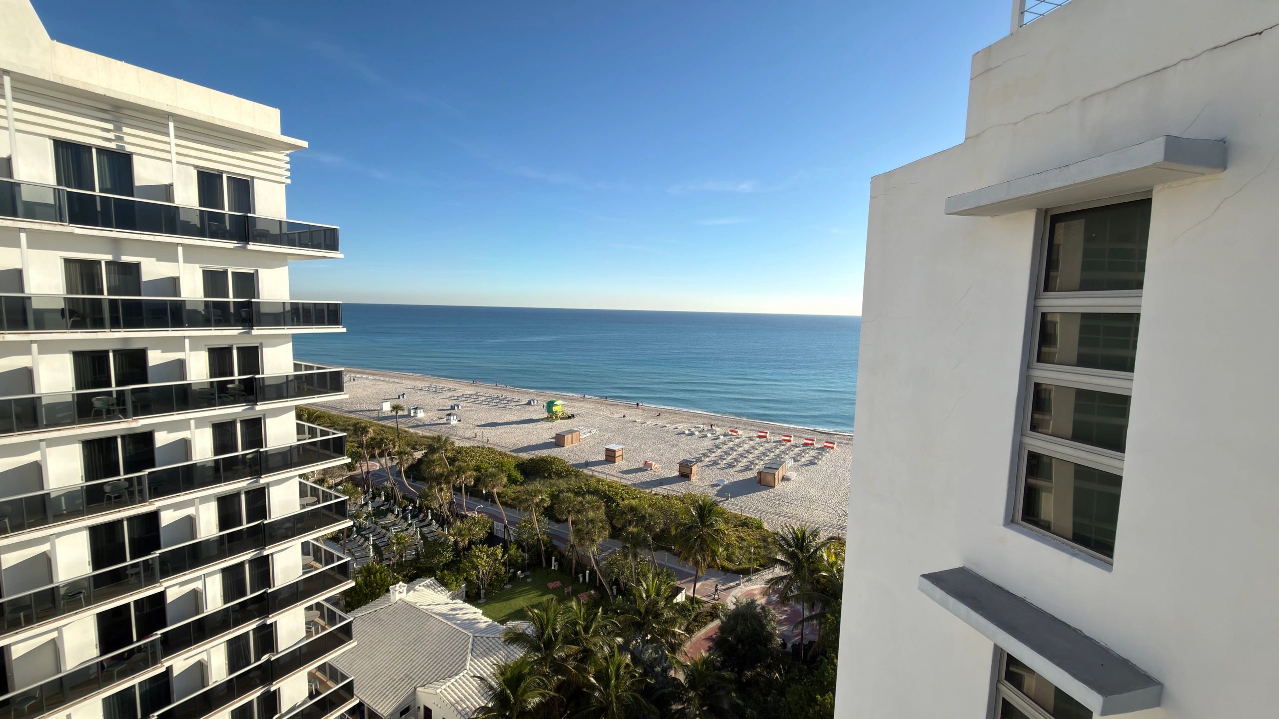 View of a beach and ocean between two white buildings under a clear blue sky.