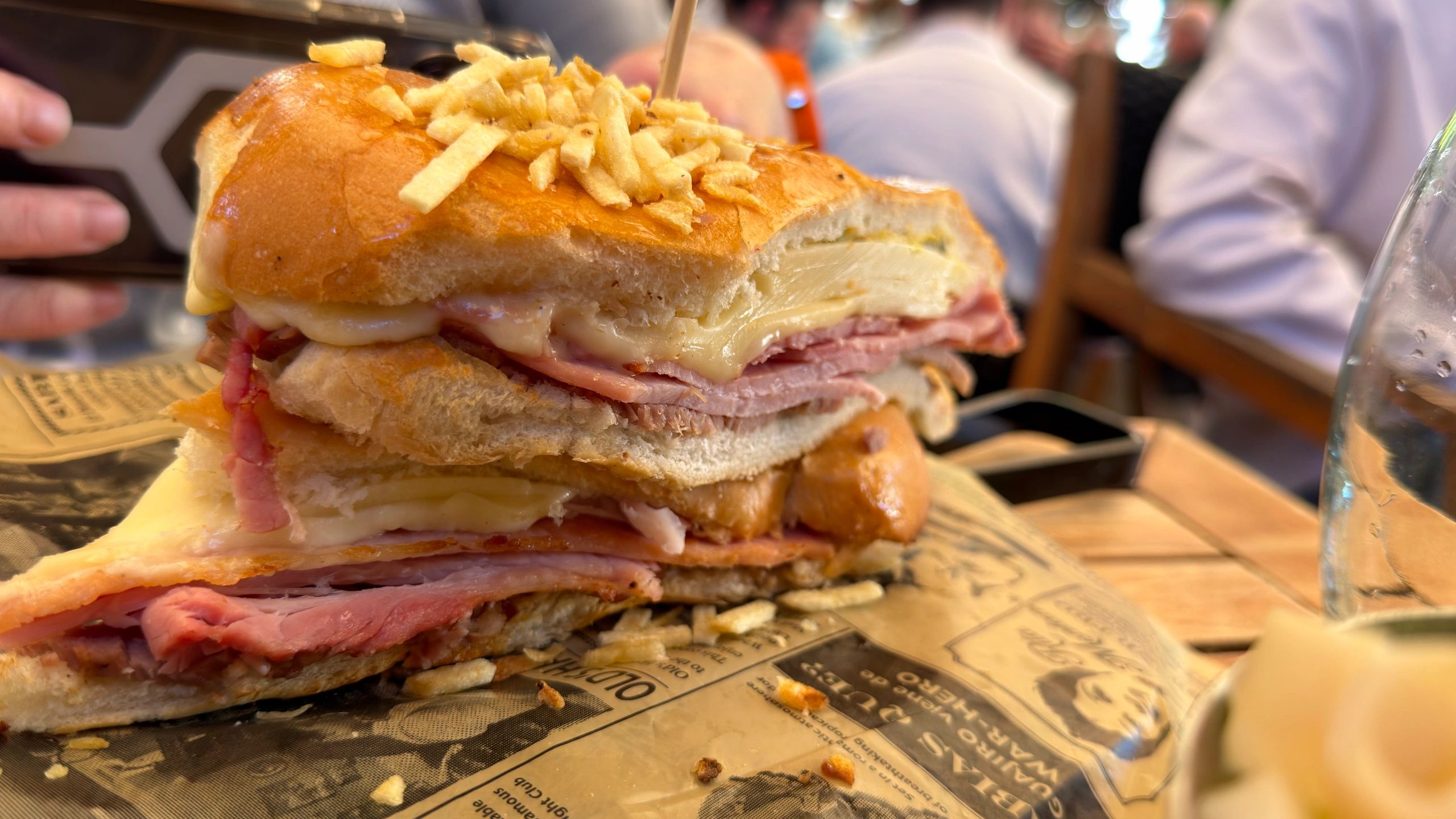Close-up of a loaded ham and cheese sandwich topped with crispy potato sticks.