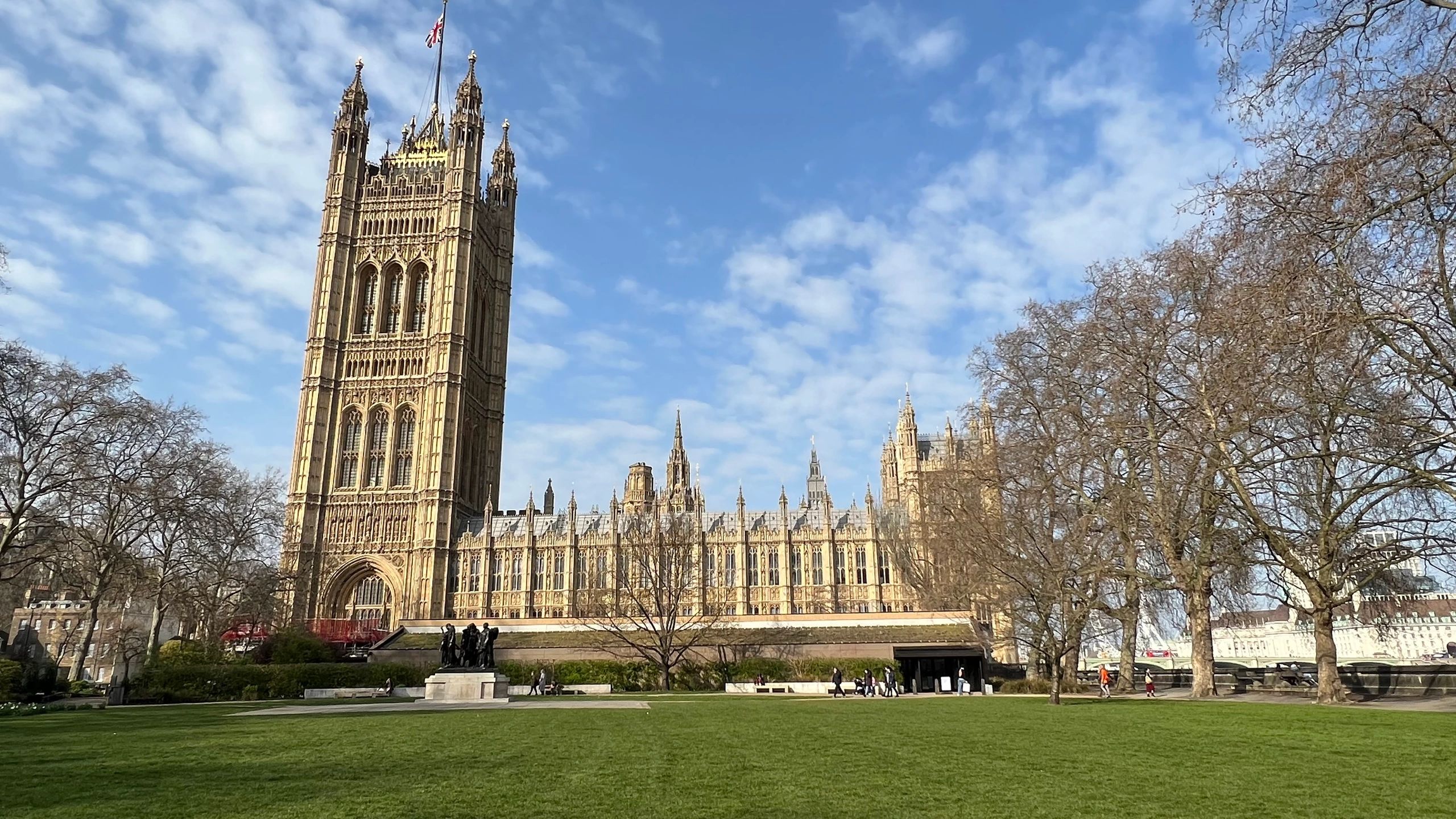 Historic UK Parliament building under a blue sky with scattered clouds.