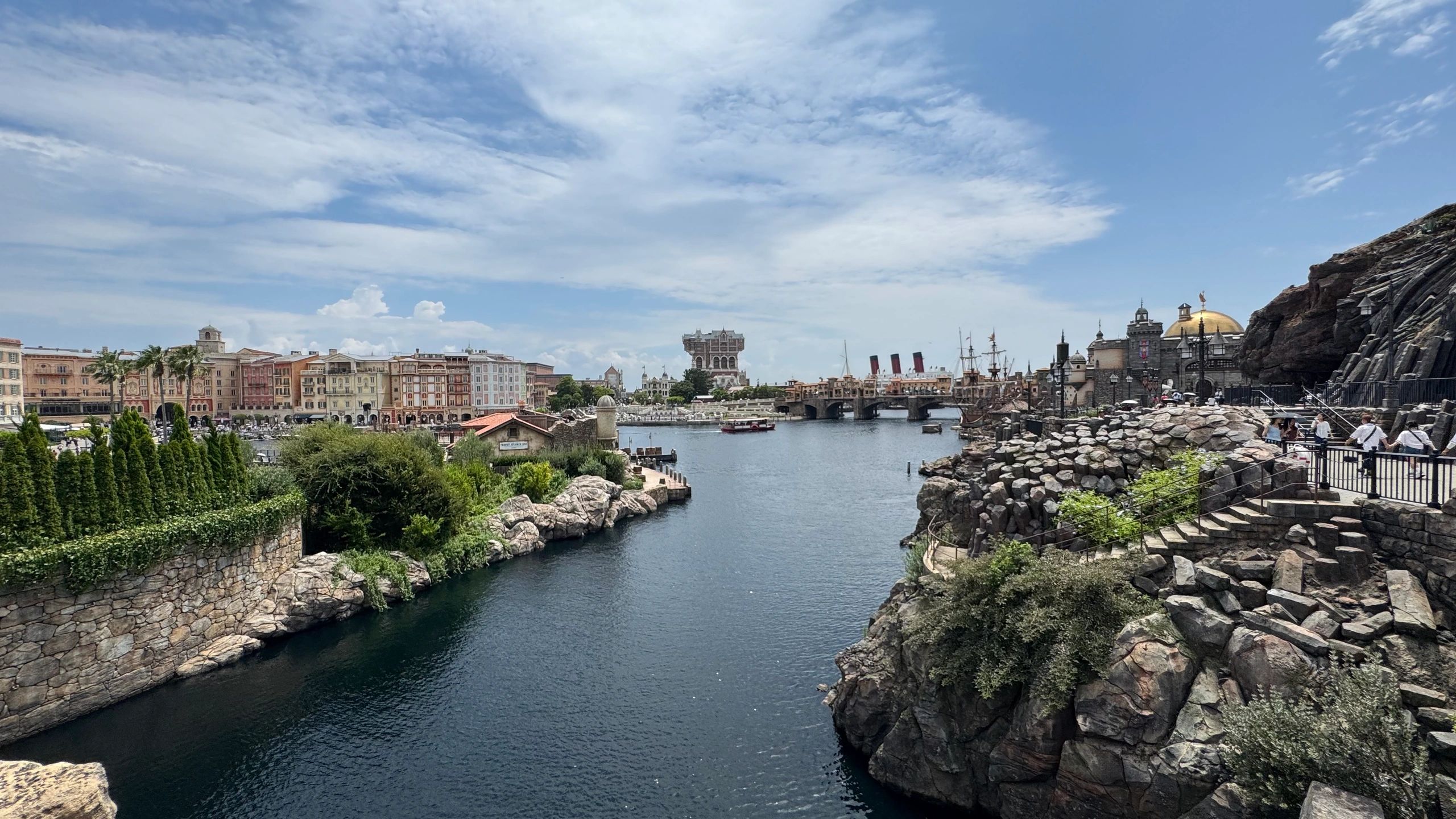 Scenic waterfront with buildings, rocky cliffs, and a partly cloudy sky.