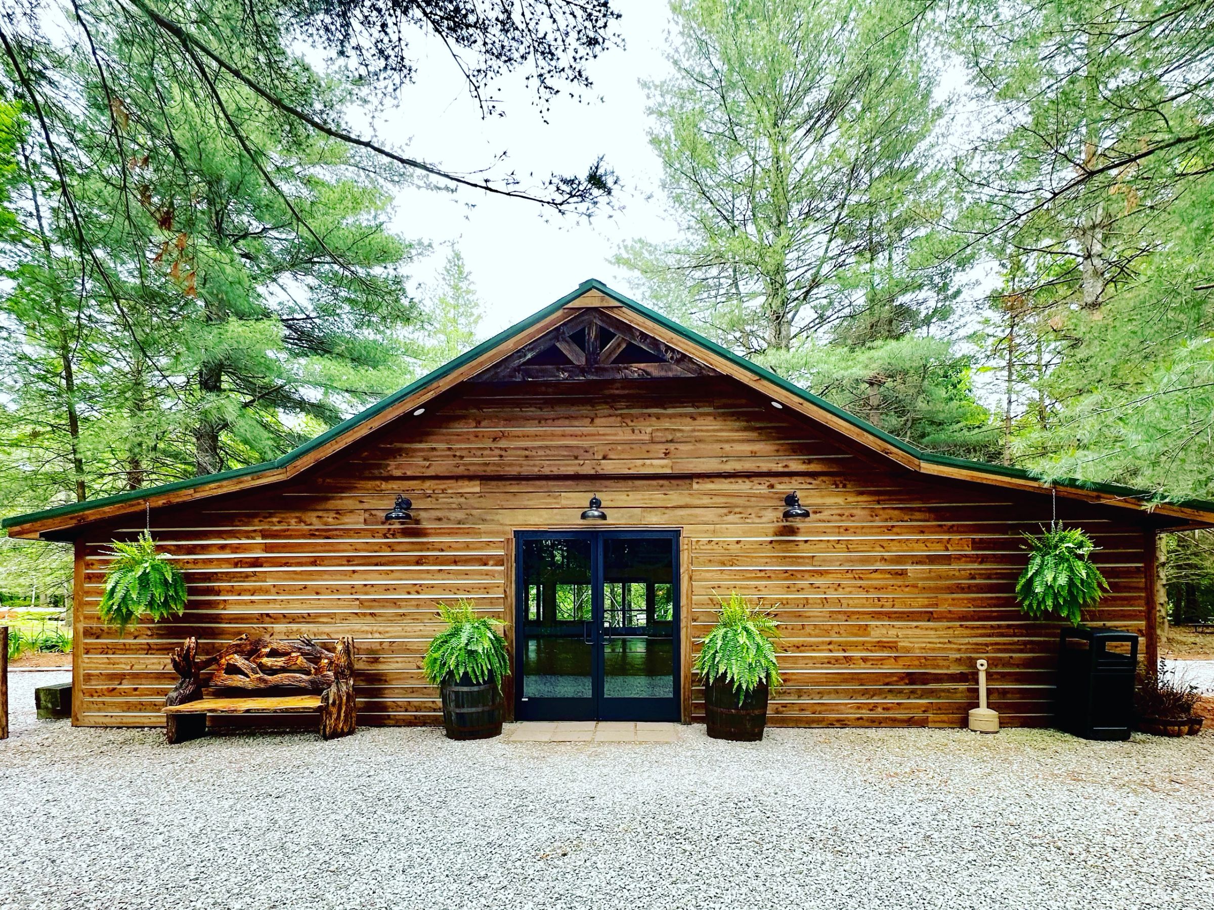 The Gables, a rustic cedar wedding venue with a green gable roof surrounded by tall pine trees in Derby, Indiana