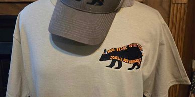 T-shirt with a bear logo and a cap hanging on a wooden surface.