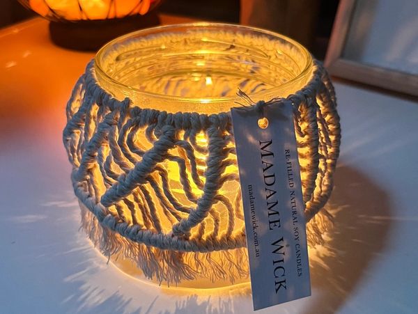 A glowing candle jar wrapped with macrame and a Madame Wick tag.