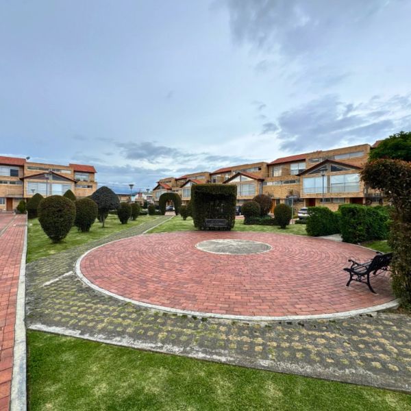 Residential courtyard with trimmed bushes and brick pathways under a cloudy sky.