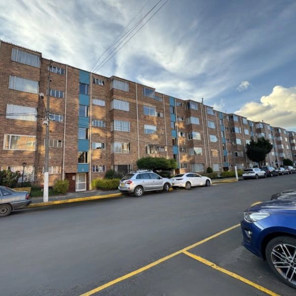 Apartment building with parked cars under a partly cloudy sky.