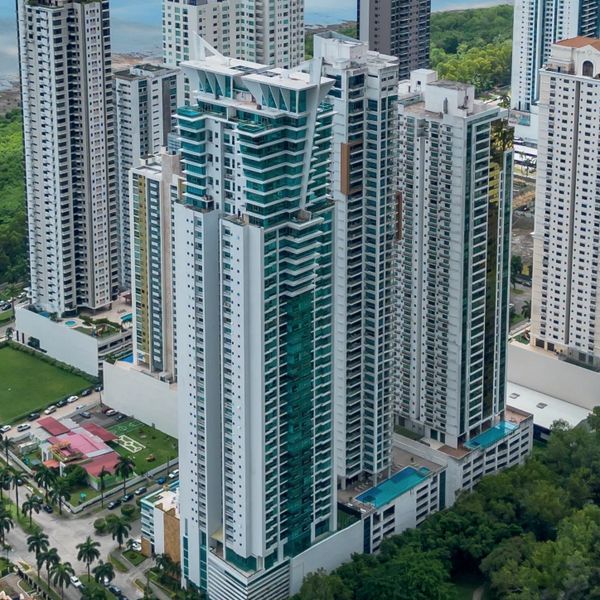 Modern high-rise buildings surrounded by greenery and water in the distance.