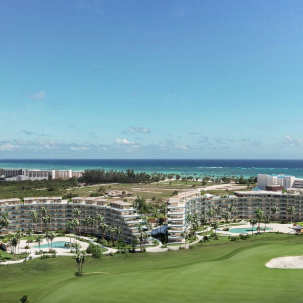 Resort buildings near a golf course by the ocean under a clear sky.