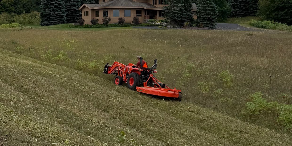 Tractor mowing grass on a slope near a house.