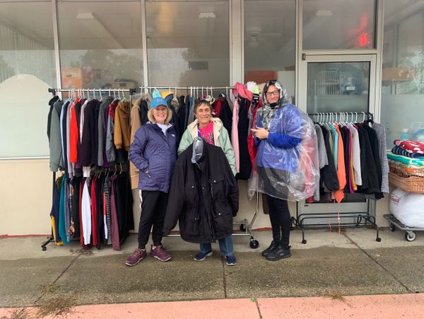 Three people standing in front of racks of coats and jackets outside a building.