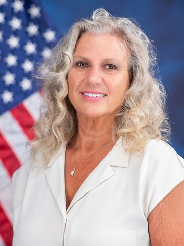 Portrait of a smiling woman with curly hair and American flag background.